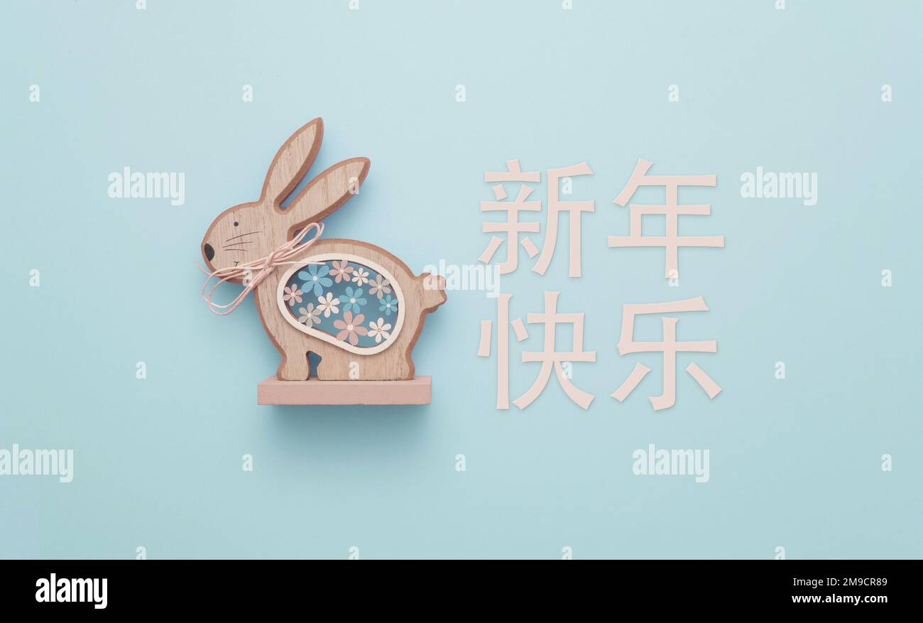 Happy Chinese New Year (新年快乐), the year of the Rabbit. A cute wooden sculpture of a rabbit against a blue background. Stock Photo