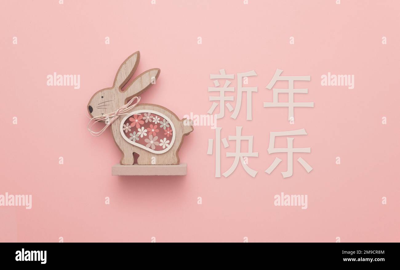 Happy Chinese New Year (新年快乐), the year of the Rabbit. A cute wooden sculpture of a rabbit against a red background. Stock Photo