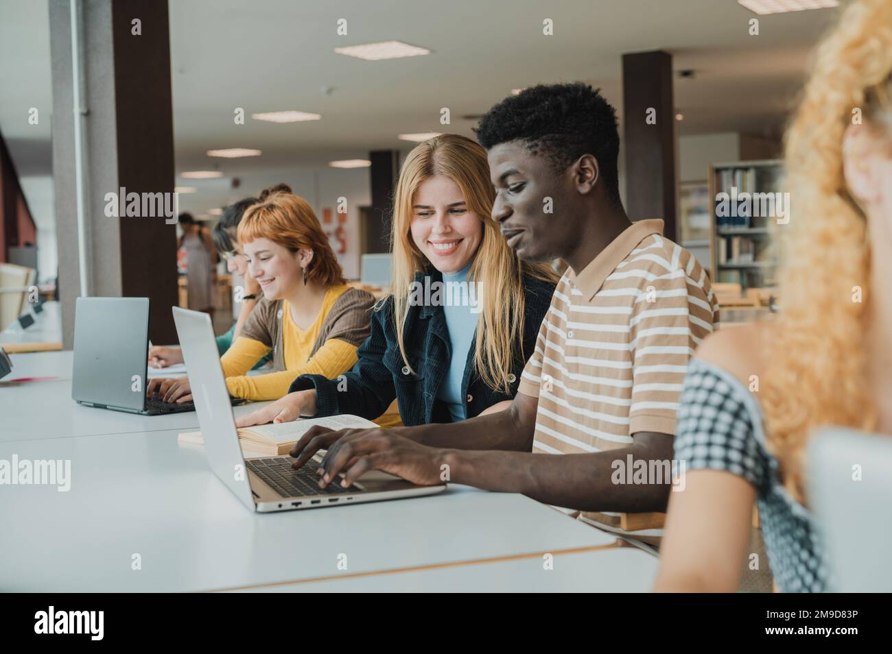Cheerful diverse friends doing assignment using laptops in university Stock Photo