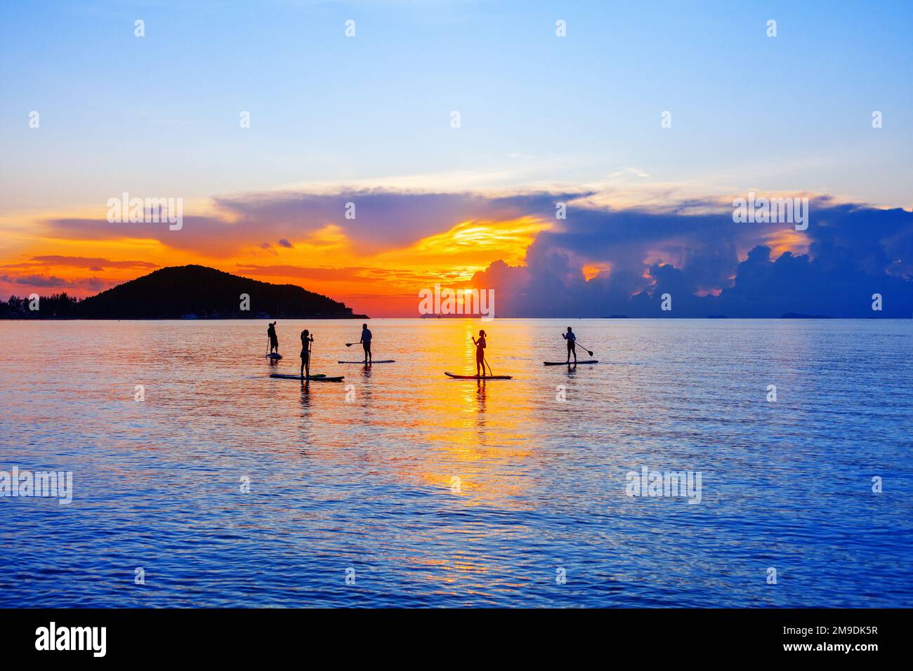 People silhouettes stand SUP paddle boarding, sea sunset beach, active young man woman surfing paddling board, ocean sunrise, surfboard, water sport Stock Photo