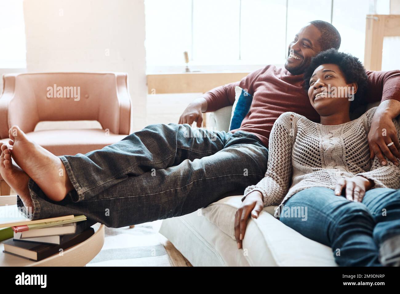 Couple, relax and watching tv on a sofa, happy and smile while bonding in their home together. Television, resting and black woman with man on a sofa Stock Photo
