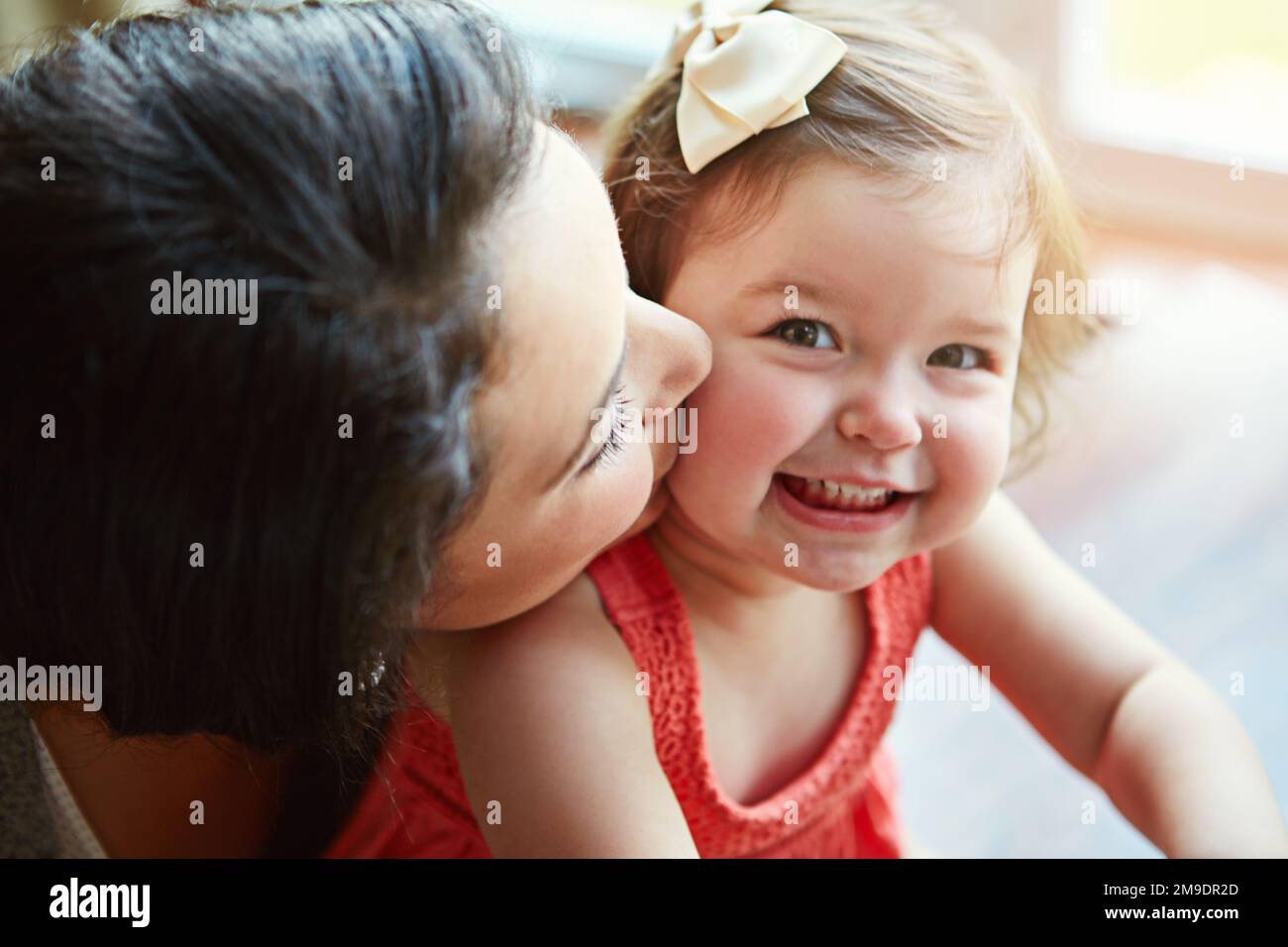 Portrait of a baby with her mother kissing her cheek while playing, bonding and spending time together. Happy, smile and girl infant child sitting Stock Photo