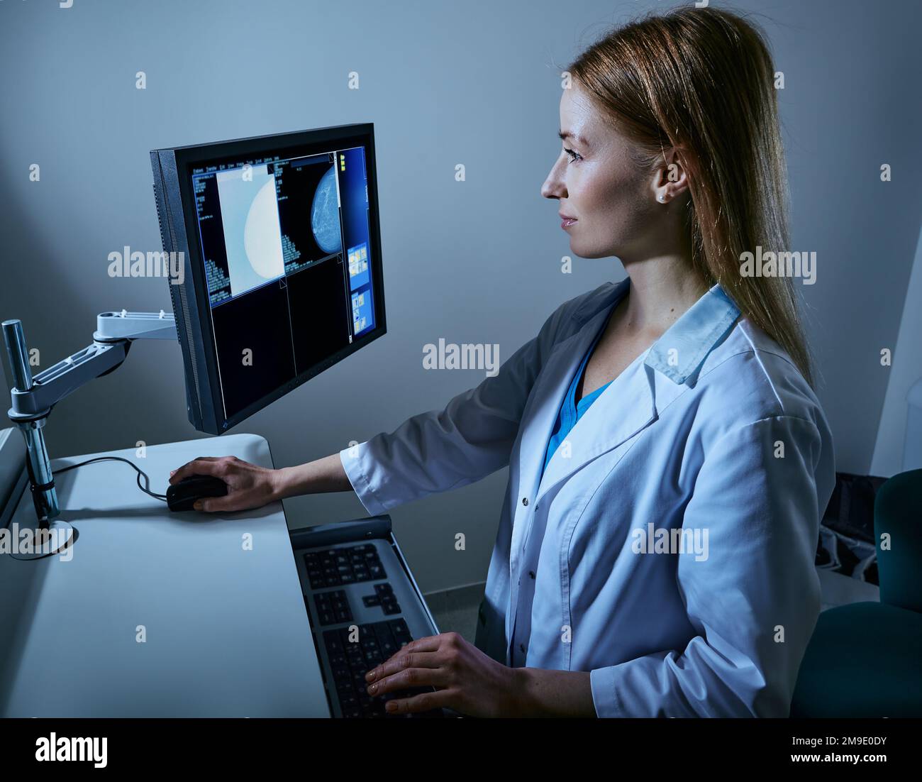 Mammogram being performed. Female medical technician looking in monitor of mammography X-ray machine and reading mammography data Stock Photo
