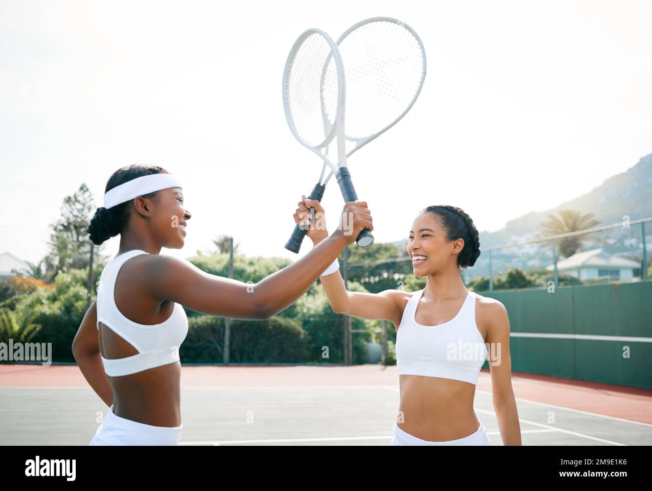 Together we are unstoppable. two sporty young women knocking their rackets together while playing tennis on a court. Stock Photo