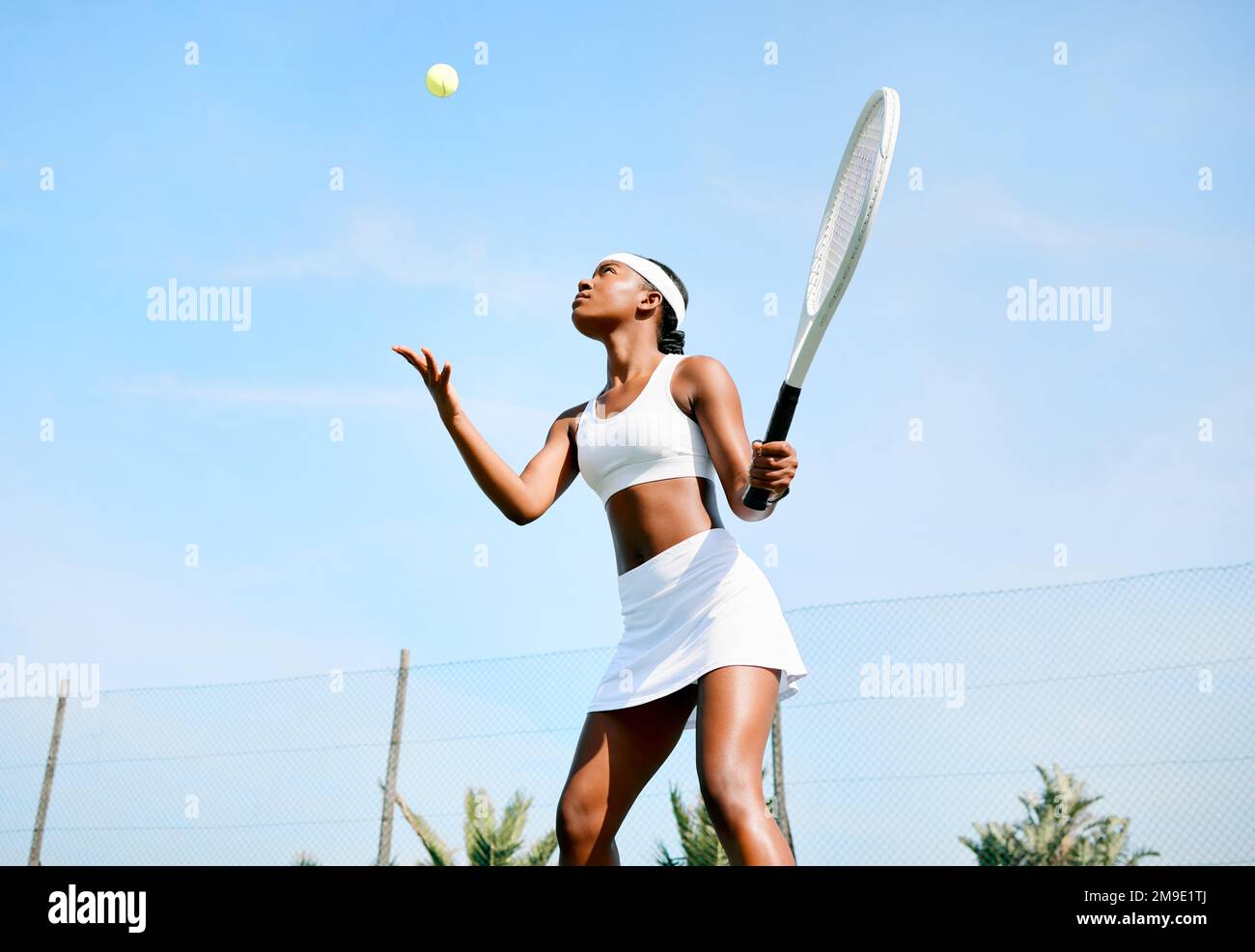 Shes ready to strike it hard. a young woman serving a ball while playing tennis on a court. Stock Photo