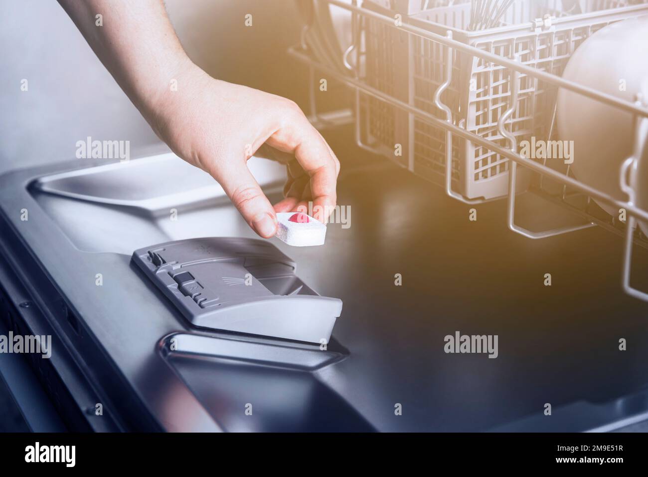 Closeup of female hand inserting dishwasher tablet into open automatic