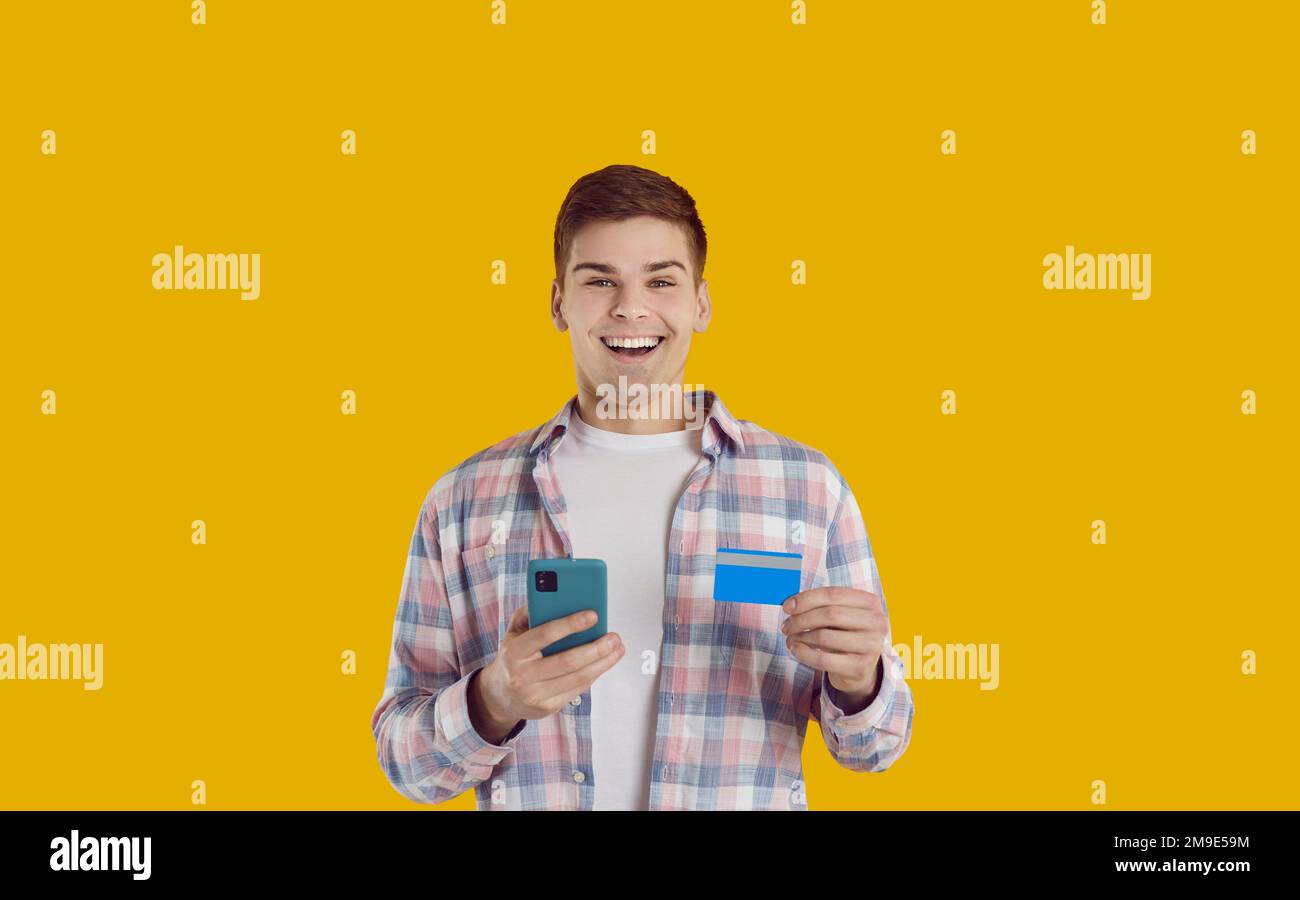 Happy young man with bank card and mobile phone shopping online or receiving payment Stock Photo