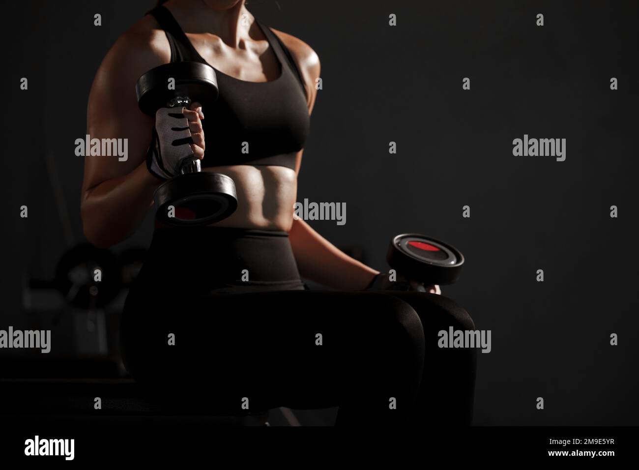Young woman lifting dumbbells for arm muscle weight training at gym. Stock Photo