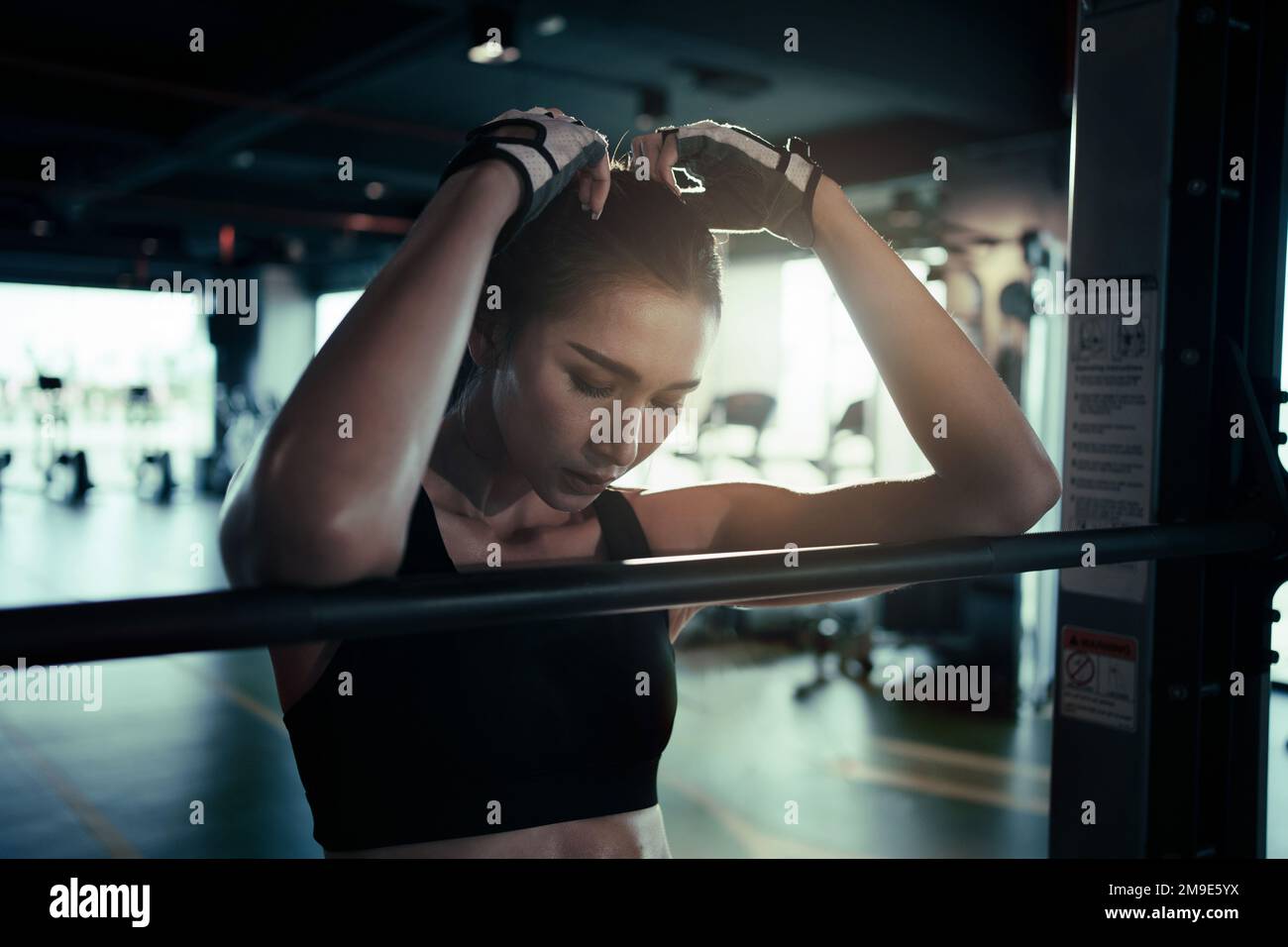Tired woman taking break after weight lifting in gym. She keeps her eyes closed. Stock Photo