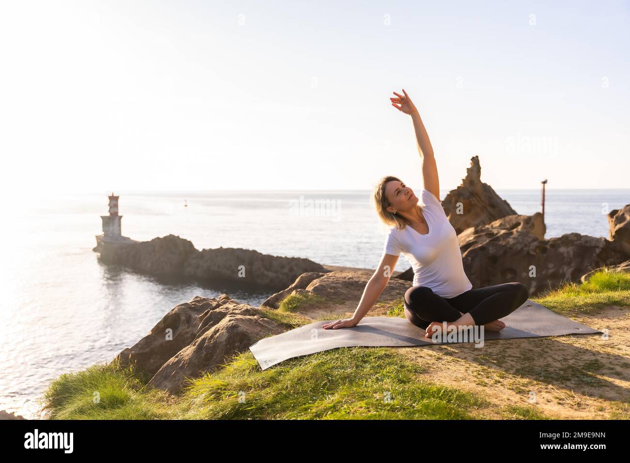 A blonde woman doing yoga exercises in nature by the sea, doing stretching Stock Photo