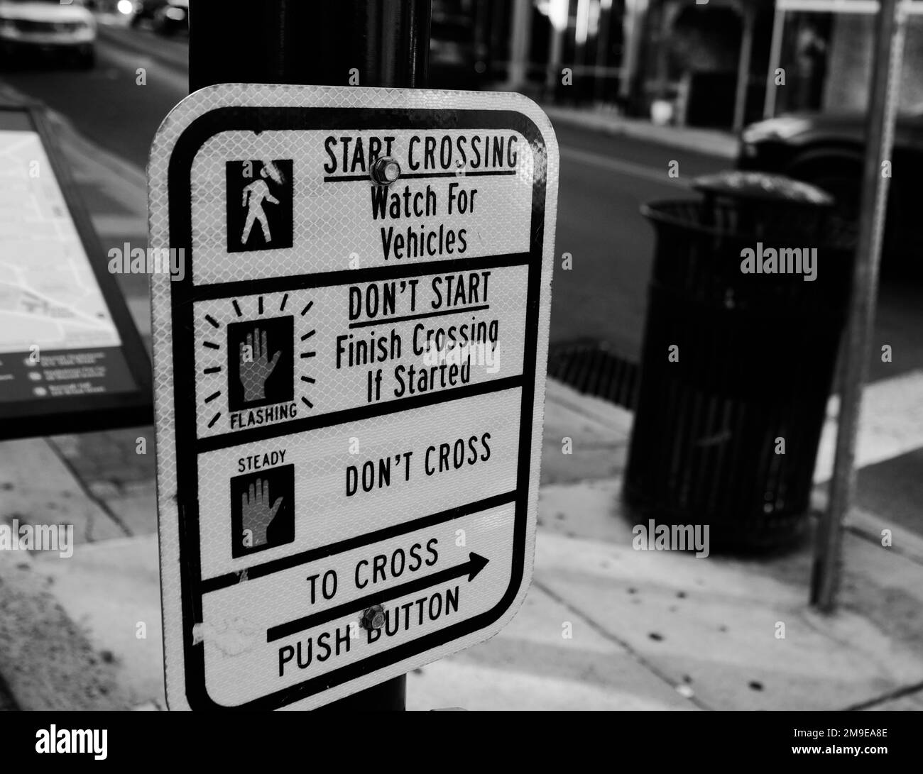 A grayscale of a street sign demonstrating the rules of crossing the