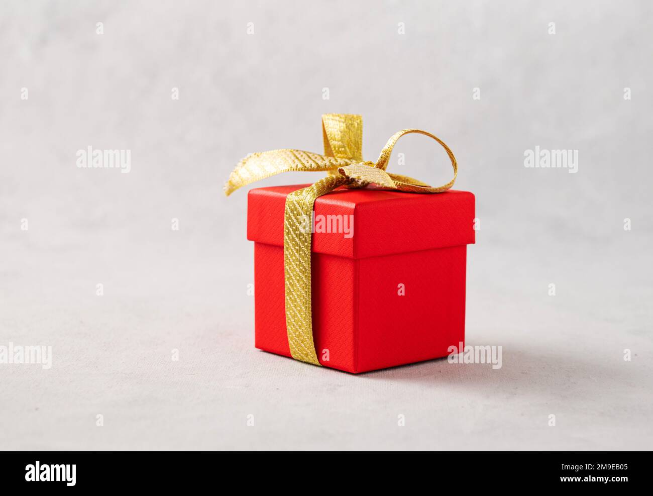 A red gift box with a gold ribbon on a gray background. The concept of holiday photography. Surprise for Valentine's Day, birthday, wedding. Copy spac Stock Photo