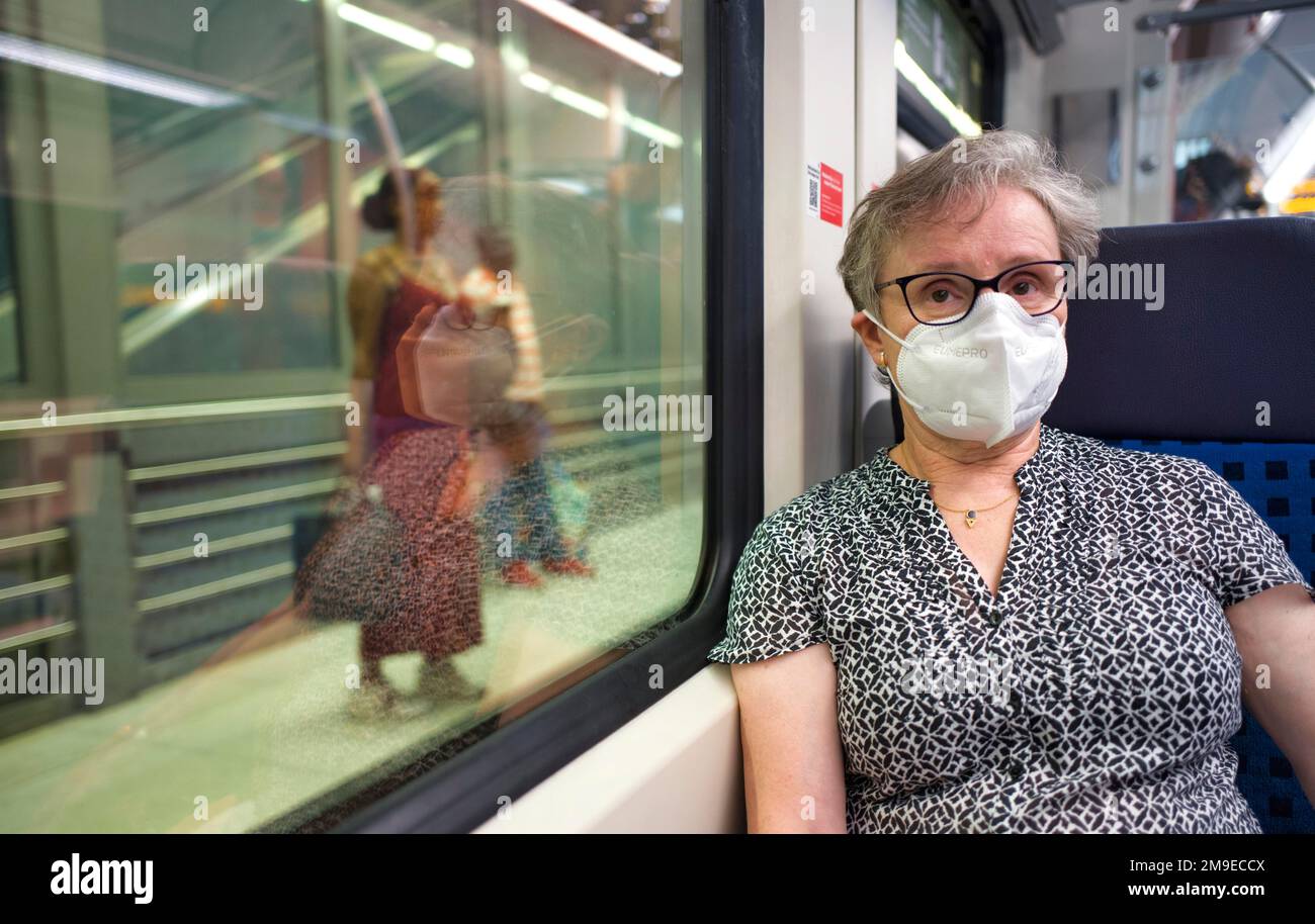 Older woman with mouth mask, sitting in S-Bahn, travellers on the platform, summer wave, Corona crisis, Stuttgart, Baden-Wuerttemberg, Germany Stock Photo
