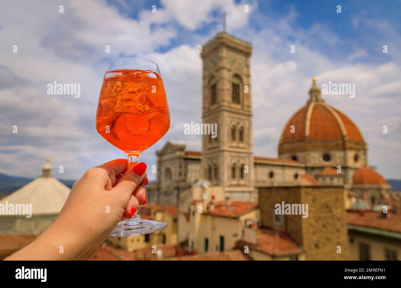 Woman s hand holding an Aperol Spritz cocktail with a view of the Duomo Cathedral or Cattedrale di Santa Maria del Fiore in Florence, Italy Stock Photo