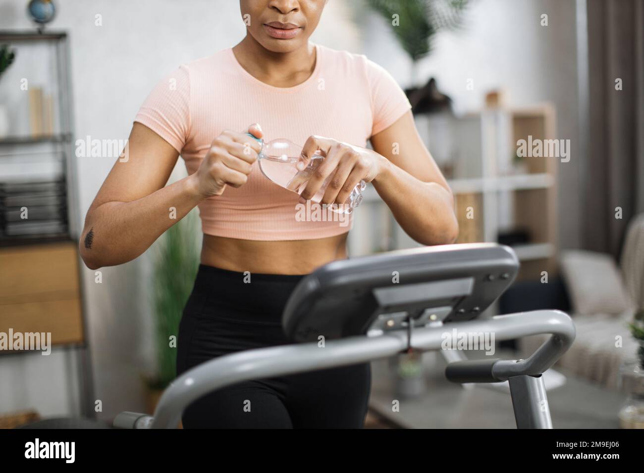 Cropped portrait of hands with bottle of water of active african american  sportive fit woman in sportswear training at home, walking, doing cardio  exercise, on treadmill Stock Photo - Alamy