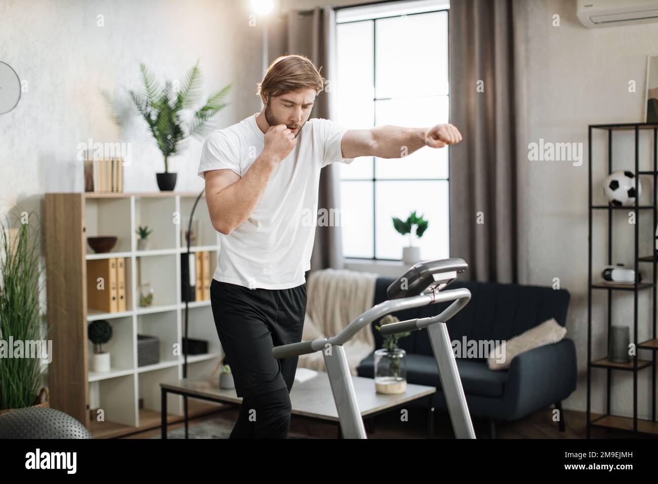 Strong young caucasian man doing boxing punches while training indoors