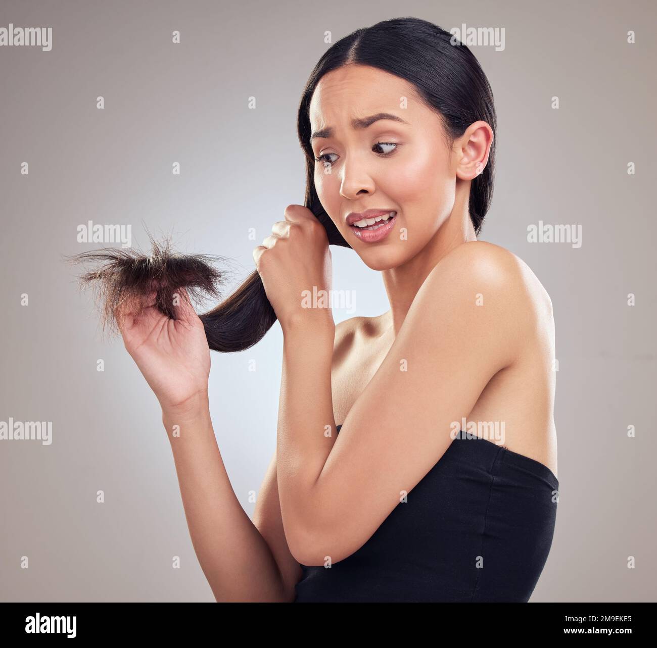 Uh oh Split ends. an attractive young woman holding her hair and looking worried while posing in the studio. Stock Photo