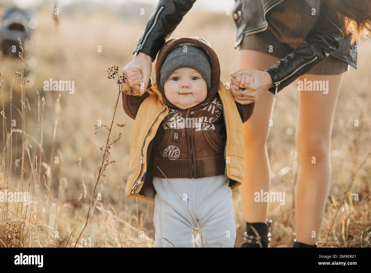 mom holds her baby boy by the hands for a walk in the fall in nature ...
