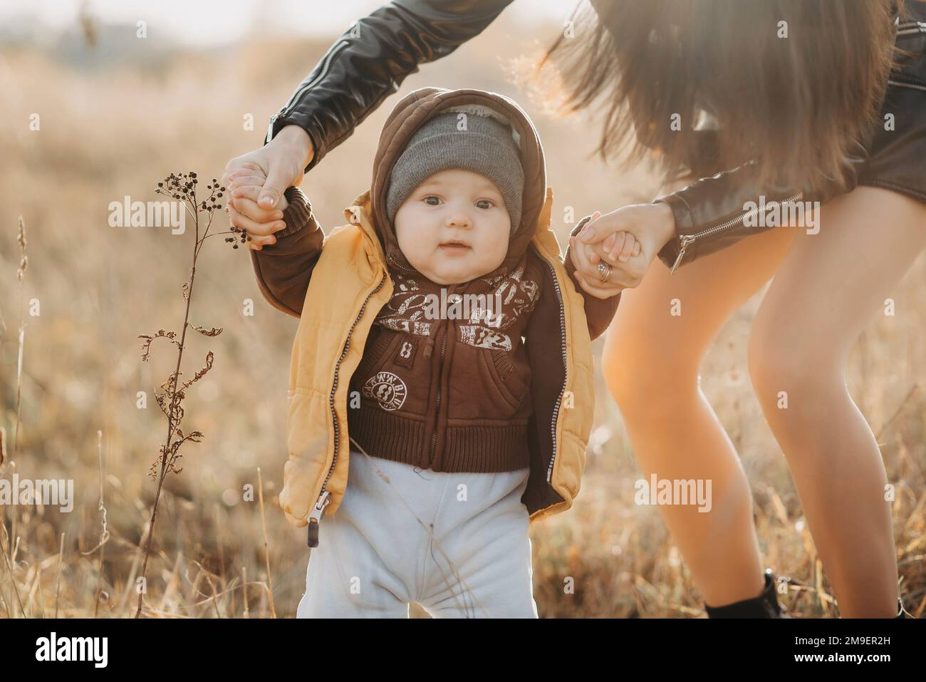 mom holds her baby boy by the hands for a walk in the fall in nature ...
