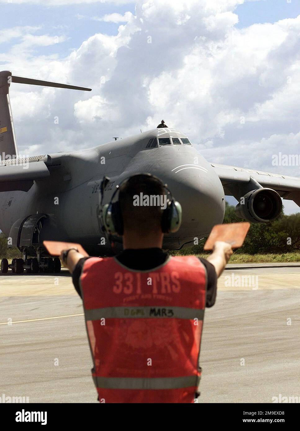 Medium shot, left front view (of aircraft), AIRMAN First Class Andre Raymundo, USAF, Crew CHIEF, 436th Aircraft Generation Squadron, Dover Air Force Base, Delaware, (back to camera) Marshalls a C-5 Galaxy from 436th Airlift Wing, South African Air Force Base Hoedspruit during Operation 'ATLAS RESPONSE', 7 March, 2000. The C-5 is delivering cargo pallets, personnel, and two HH-60 Blackhawk Helicopters, from the 41st Rescue Squadron at Moody Air Force Base, Georgia The Personnel and Helicopters are the first American HH-60's delivered to aid in the distribution of relief supplies and rescue stra Stock Photo
