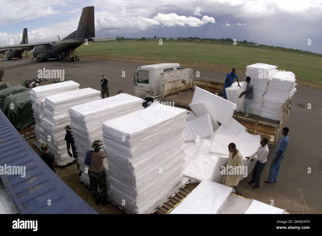 A medium shot from a high angle looking down as US Air Force members of the 86th Air Mobility Squadron, Ramstein Air Base, Germany, with help from local Laborers, build pallets of bedding material to be transported to various locations in Mozambique at the International Airport at Maputo, Mozambique, Africa on 16 March 2000. They and their team are deployed here in support of Operation Atlas Response, a Humanitarian Aid Operation to help the people of Mozambique, after severe flooding (flooding and victims not shown) displaced over a million people from their homes. Subject Operation/Series: A Stock Photo