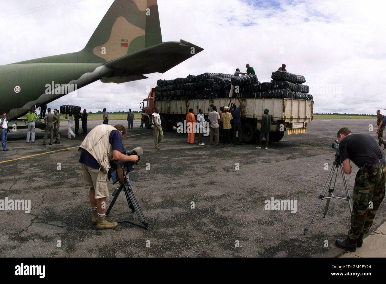 Medium long shot. A Portugese Aircrew and local laborers, load humanitiarian reilef supplies onto a Portugese C-130 at the International Airport at Maputo, Mozambique, Africa, on 17 March 2000, as Glen Felgate, a Videographer, from Reuters News Service, and Technical Sergeant John Trautt, a Videographer from the 786th Communications Squadron, Ramstein Air Base, Germany, document the operation. The aircraft and its crew are deployed to Maputo, in support of Operation Atlas Response, a Humanitarian Aid Operation to help the people of Mozambique, after severe flooding displaced over a million peo Stock Photo