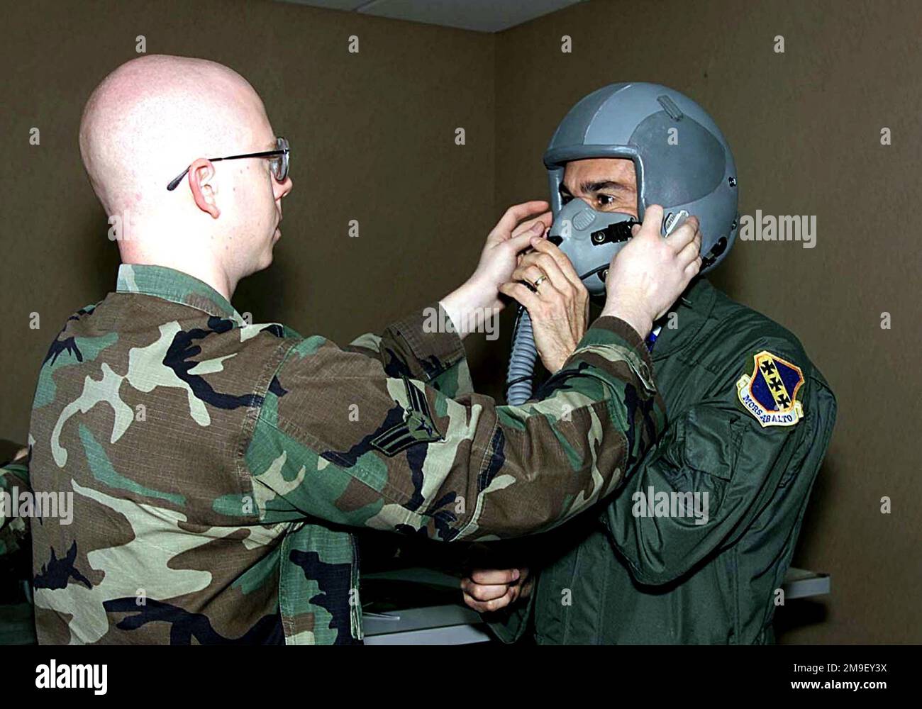 Medium close shot. Mr. McKee (right) gets fitted for his gas mask