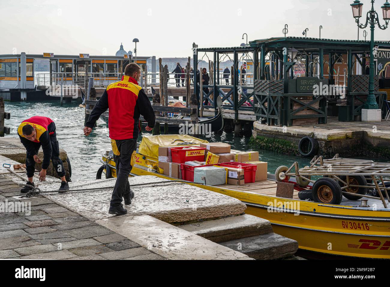 Two couriers deliver packages on a DHL boat on the Grand Canal in Venice. Stock Photo