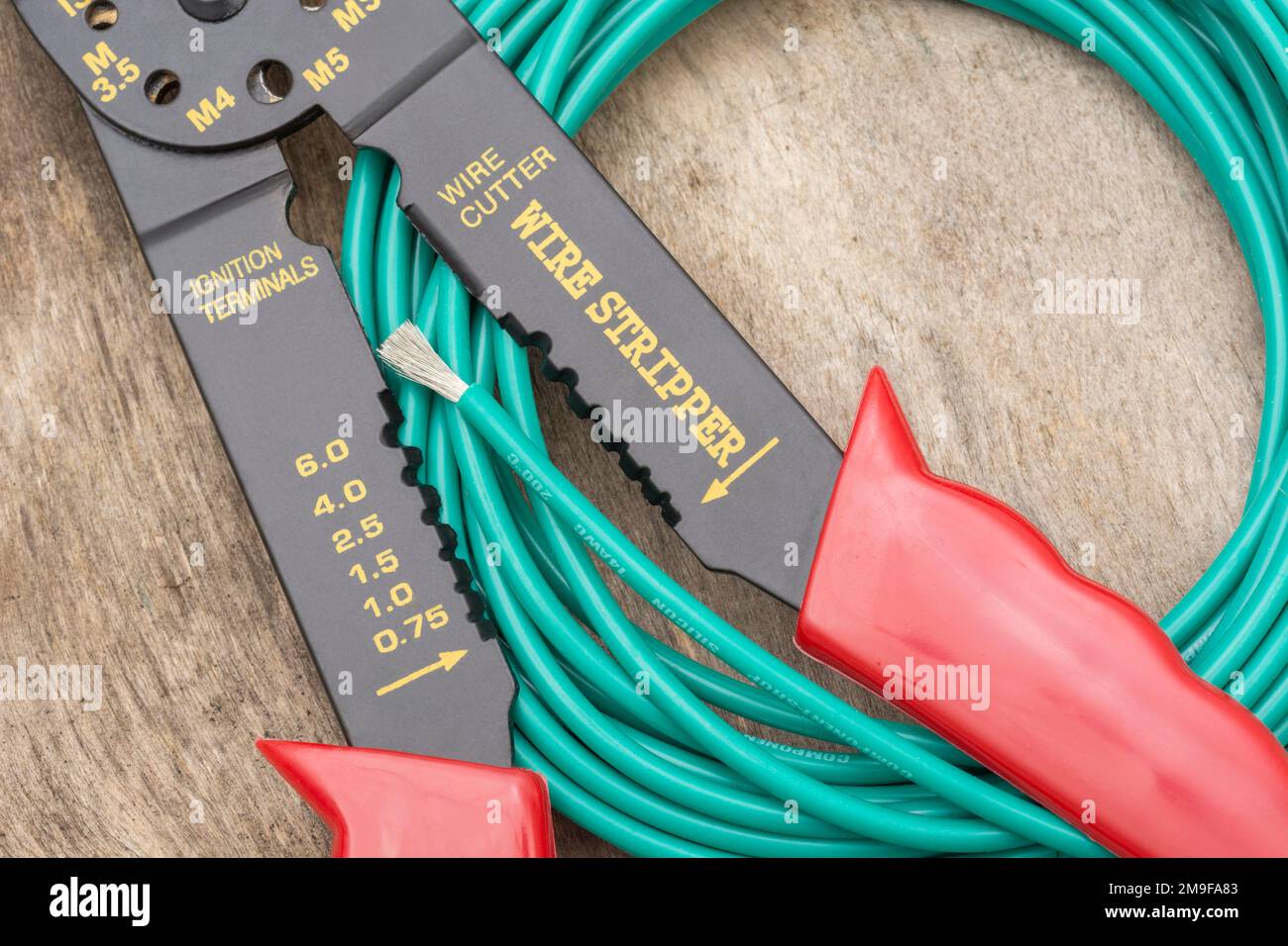 Close shot of Chinese made unbranded wire stripper & wire cutter for 26-10AWG wire (see Notes) with coiled role of green silicone covered wire. Stock Photo