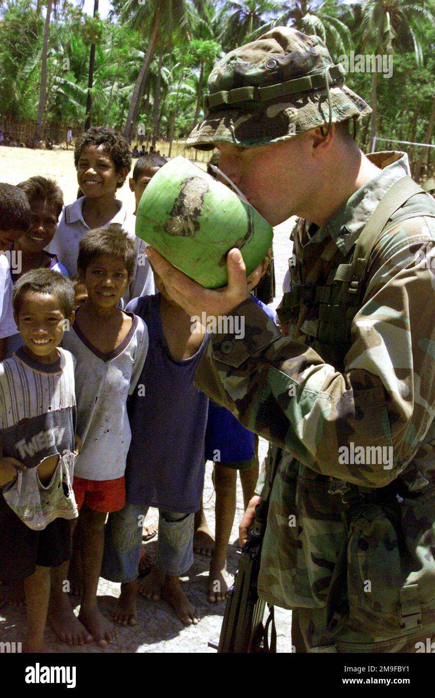 US Marine Lance Corporal Gregory Hughes, a SAW (Squad Automatic Weapon) GUNNER with Third Platoon, India Company, Battalion Landing Team 3/1, 13TH Marine Expeditionary Unit (Special Operations Capable), stops for a refreshing drink from a coconut that the local children offered with gratitude during a Humanitarian Assistance Operation, East Timor, September 2000. US Marines and Sailors from Tarawa Amphibious Ready Group spent three days in East Timor providing Medical and Community Relations Services to help rebuild the war torn nation. Subject Operation/Series: HUMANITARIAN ASSISTANCE OPERATI Stock Photo