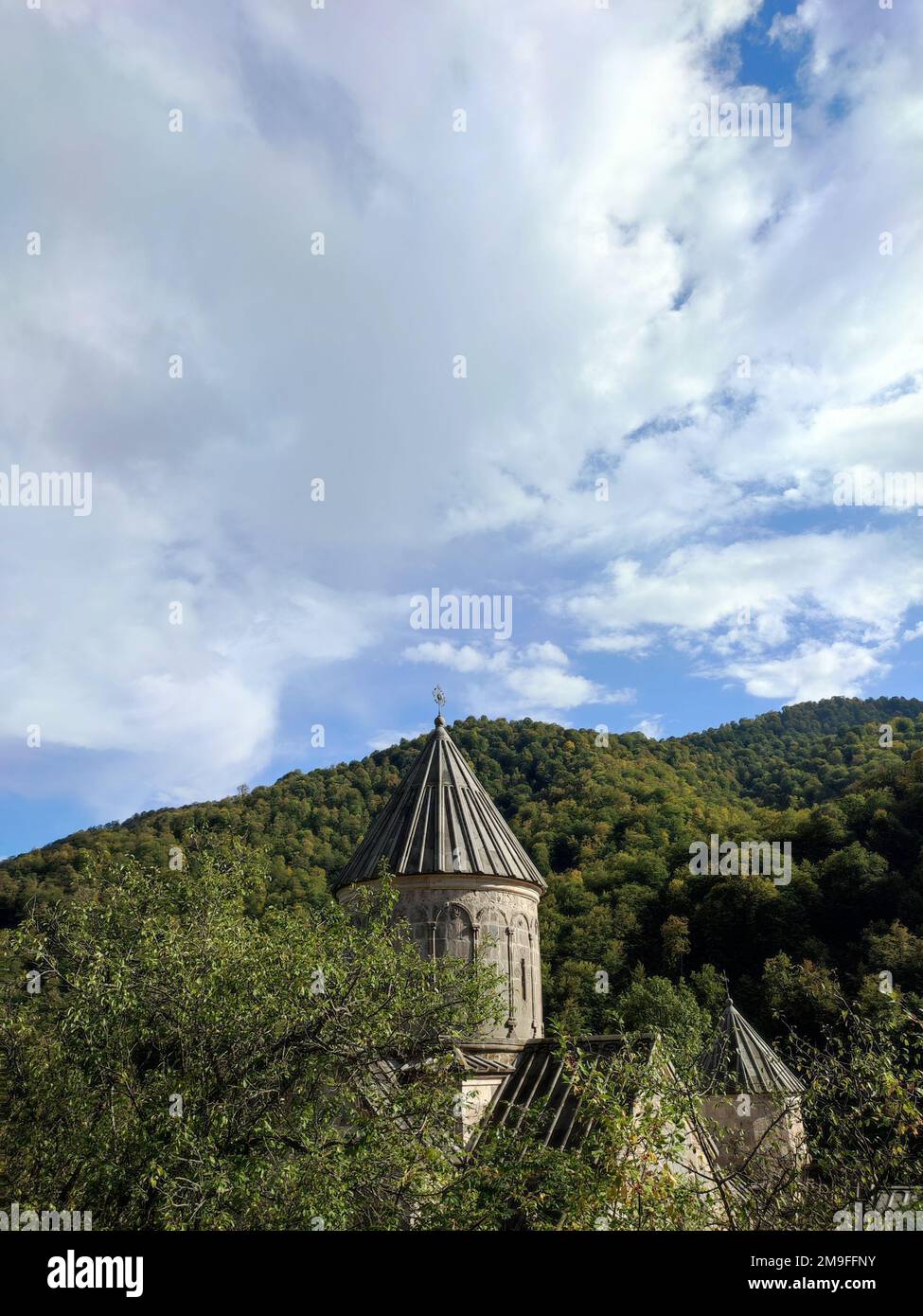 A vertical shot of the dome of the Haghartsin Monastery in Tavush, Armenia, seen behind lush trees Stock Photo