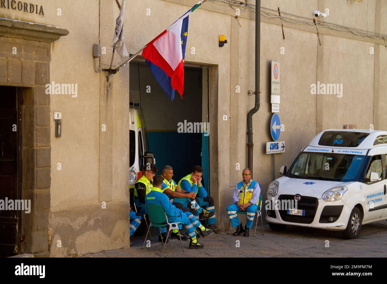 Ambulance personnel, taking a break at their post, next to an ambulance, under an Italian flag Stock Photo