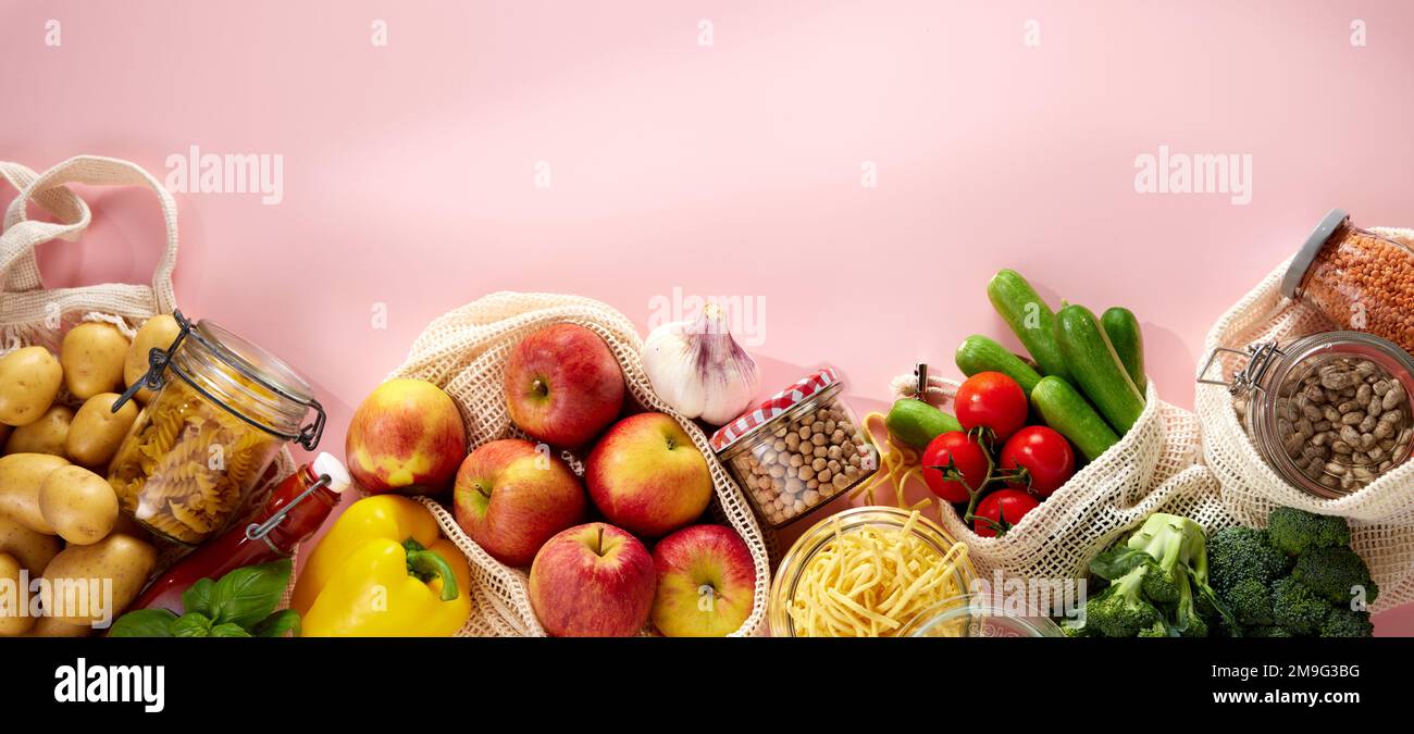 Top view of appetizing fresh raw apples potatoes cherry tomatoes cucumbers broccoli and yellow bell pepper in eco friendly cotton sacks placed on pink Stock Photo