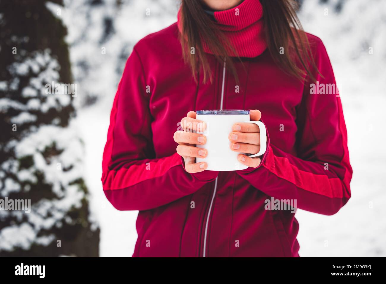 Unrecognizable woman in red winter jacket holding a tea cup while standing in a snowy winter forest Stock Photo