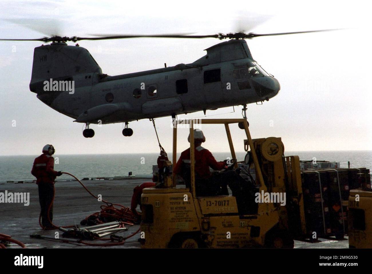 US Navy Aviation Ordnancemen hook ordnance containers to an CH-46D Sea ...