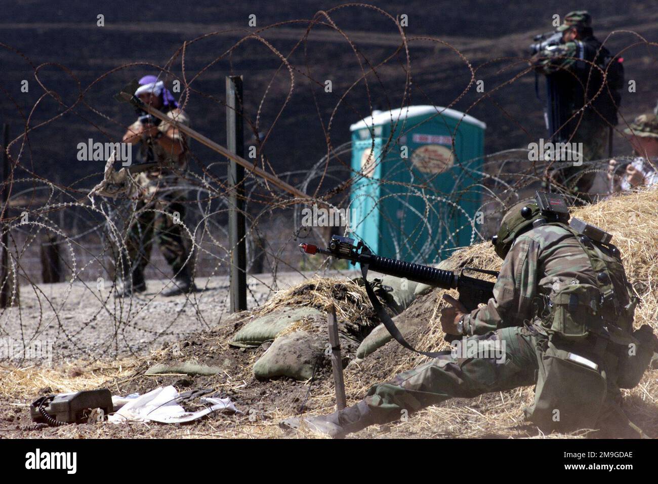 A soldier tries to take cover when oppostion Forces storm the entry control point, while Henry Guardado of the 4th Combat Camera, March ARB, California, documents all the action. Reserve forces from all over the nation are participating in Operation GOLDEN MEDIC 2001, a multi-unit, medical, field training exercise held at Parks Reserve Forces Training Area, Dublin, California, in which the Army transports simulated casualties from the frontline through various staging areas to a main tent in order to train personnel in medical procedures and evacuation methods. Attached to the helmet, upper bo Stock Photo