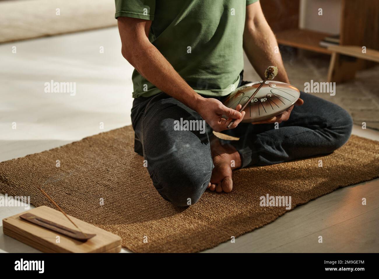 Closeup of yoga man sitting in lotus position on carpet and using fimbo in his practice Stock