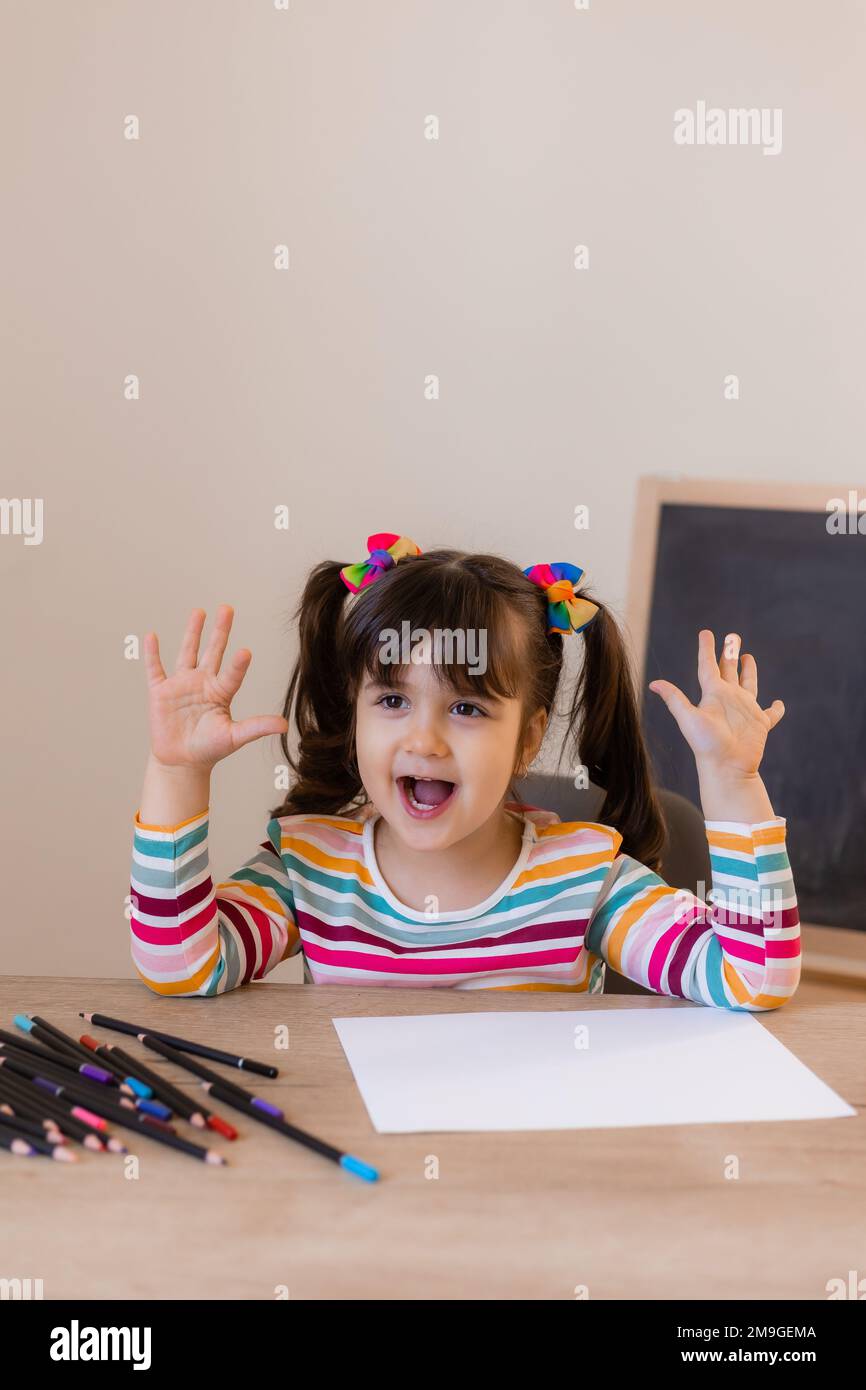 a happy cute little girl in a drawing lesson raises her hand at the top Stock Photo