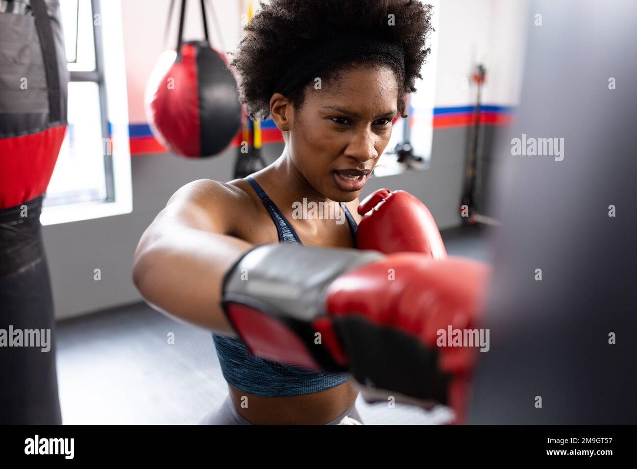 African american fit woman exercising and punching boxing bag at gym