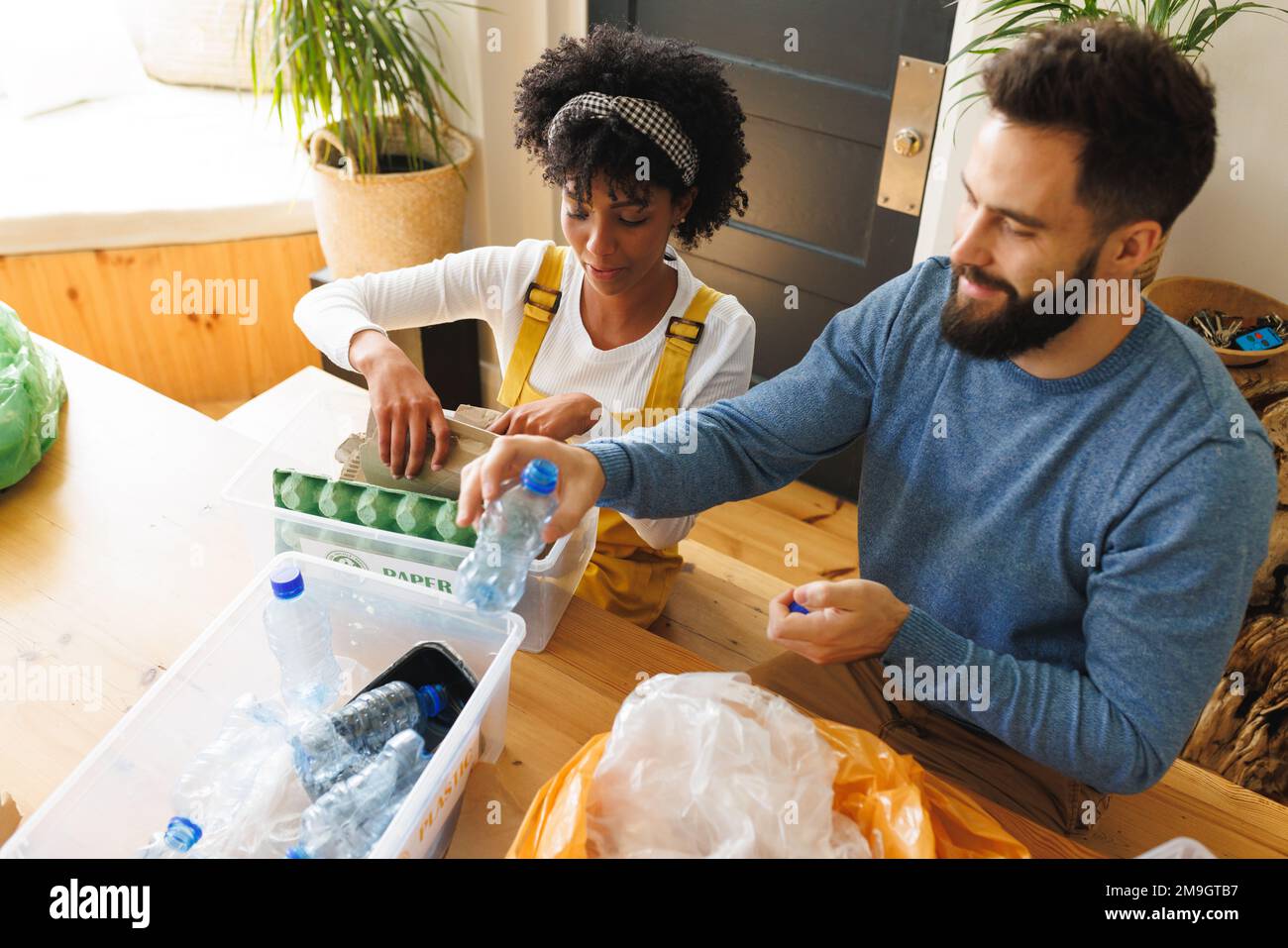 High angle view of biracial young couple sorting papers and plastics garbage in bins on table Stock Photo