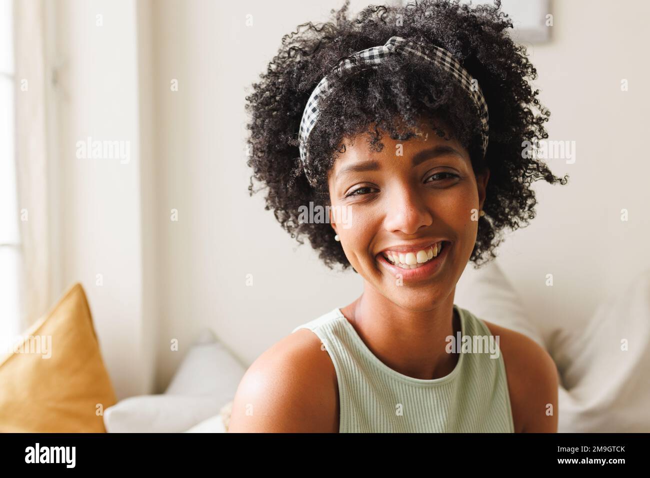 Close-up portrait of beautiful biracial smiling young woman with afro hair against wall at home Stock Photo