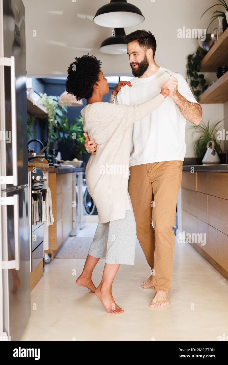 Full length of biracial young couple dancing romantically in kitchen at night, copy space Stock Photo
