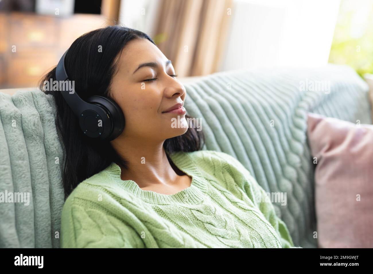 Image of happy biracial woman in headphones relaxing on sofa with eyes closed at home, copy space Stock Photo