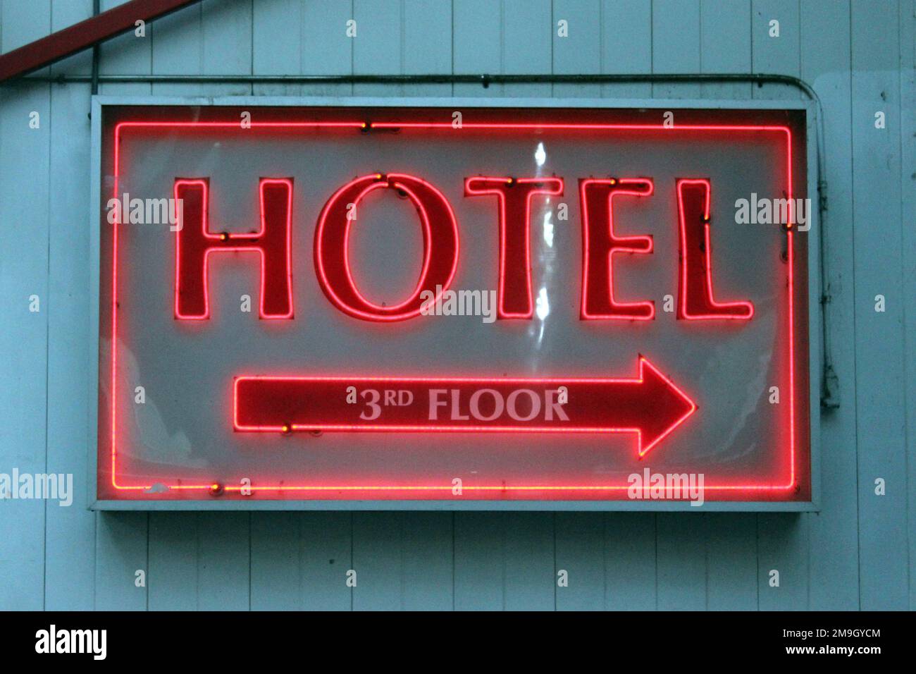A closeup of the neon Hotel sign pointing to the 3rd floor hanging from the wall Stock Photo