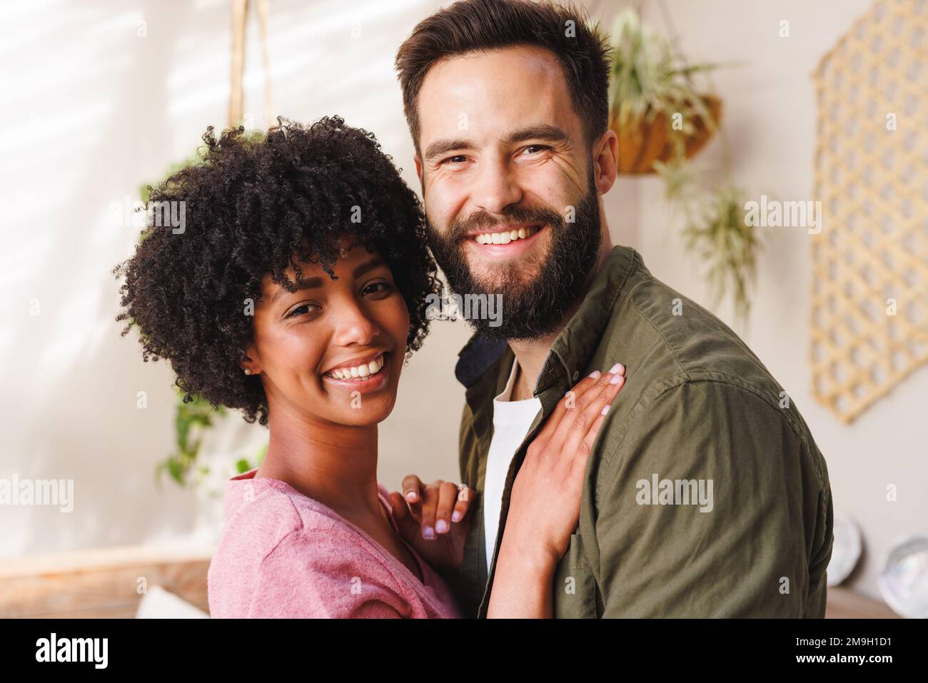 Close-up portrait of cheerful biracial young couple hugging against white wall, copy space Stock Photo