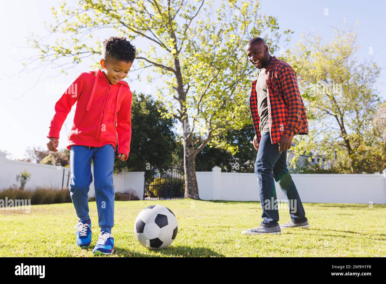 Happy african american father and son playing football in their ...