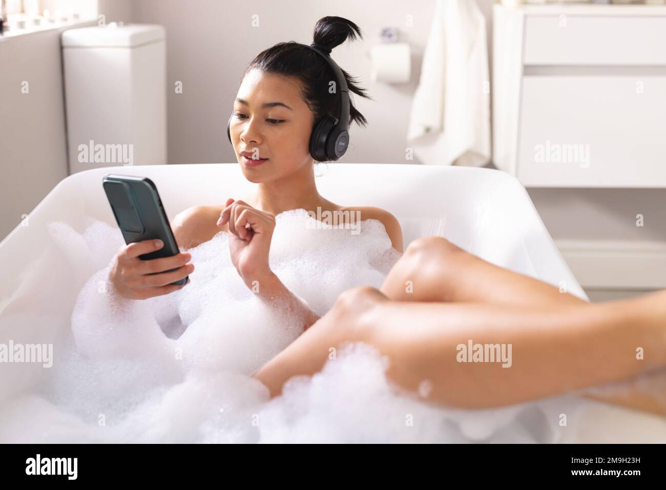 Image of biracial woman relaxing with headphones and smartphone in