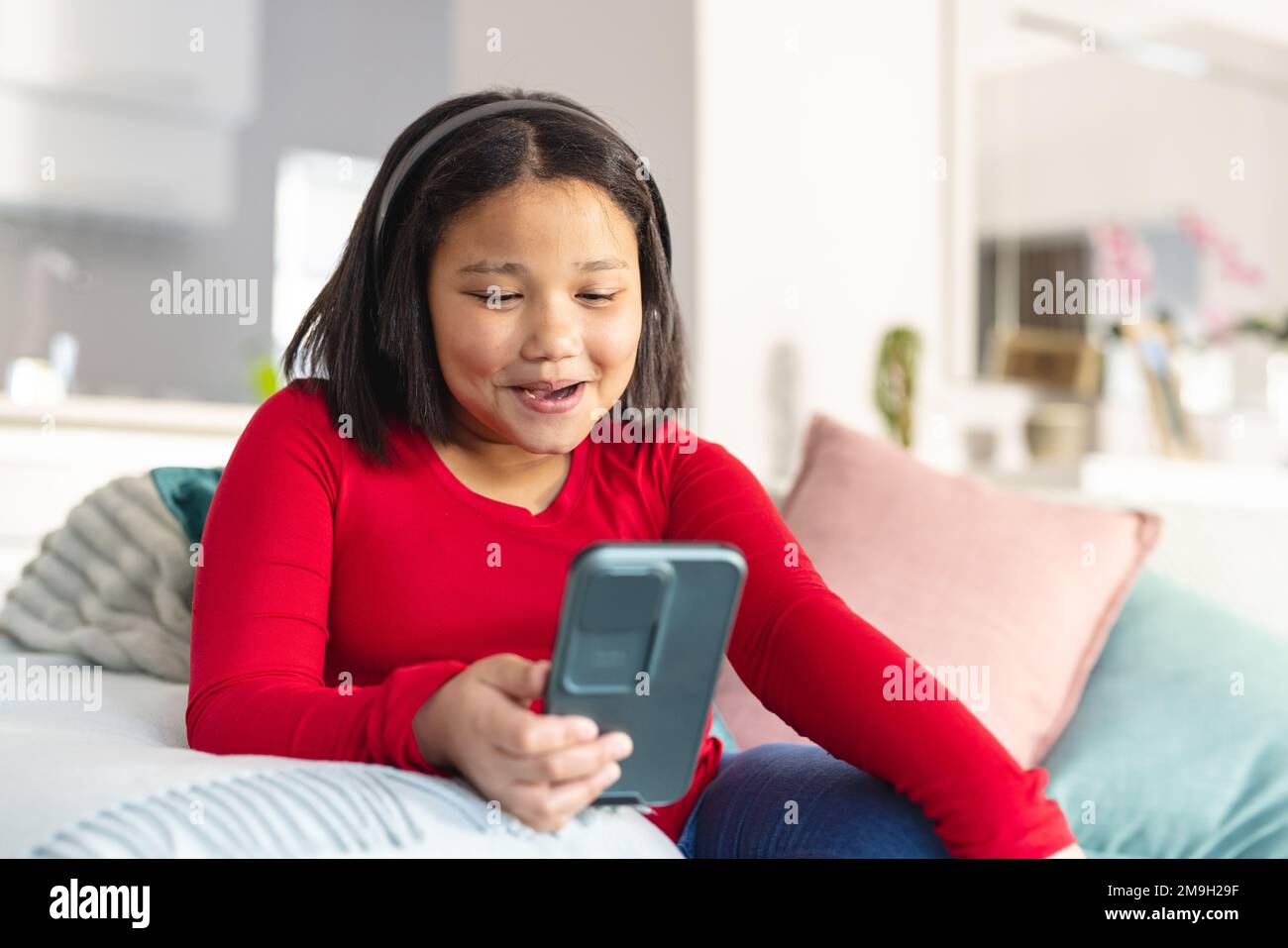 Happy asian girl sitting on sofa in living room and using smartphone ...