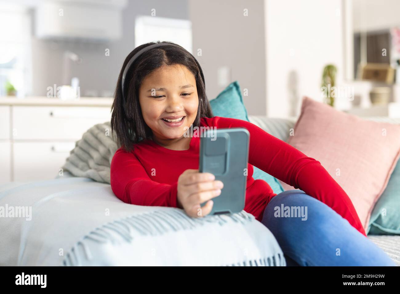 Happy asian girl sitting on sofa in living room and using smartphone ...