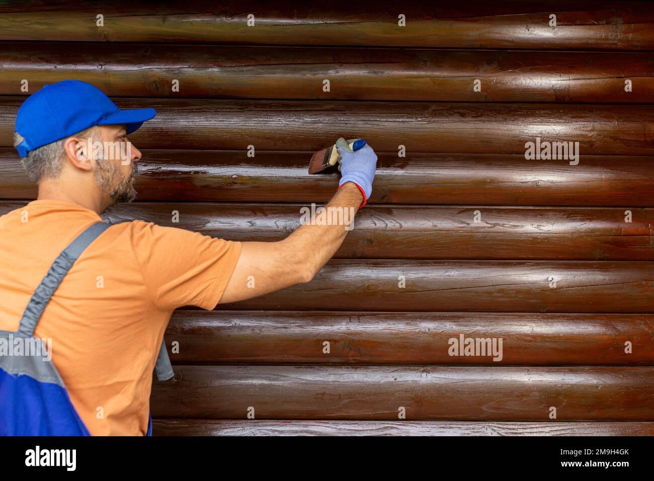 Wooden house maintenance concept. Man staining wall siding trunk Stock